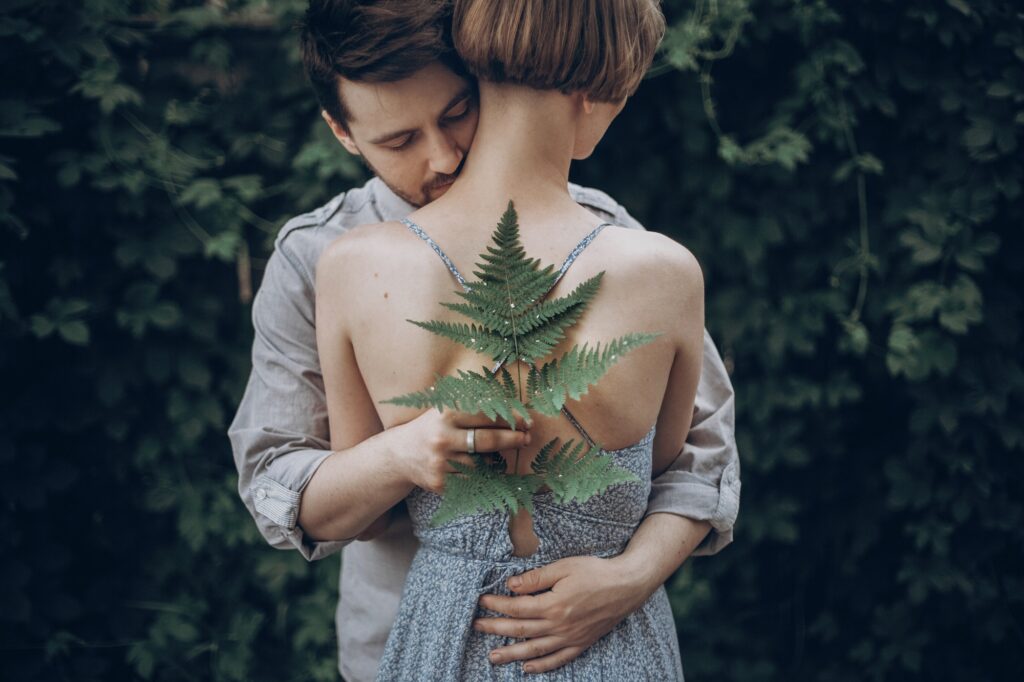 stylish hipster bride and groom embracing in green leaves forest man kissing woman neck.jpg