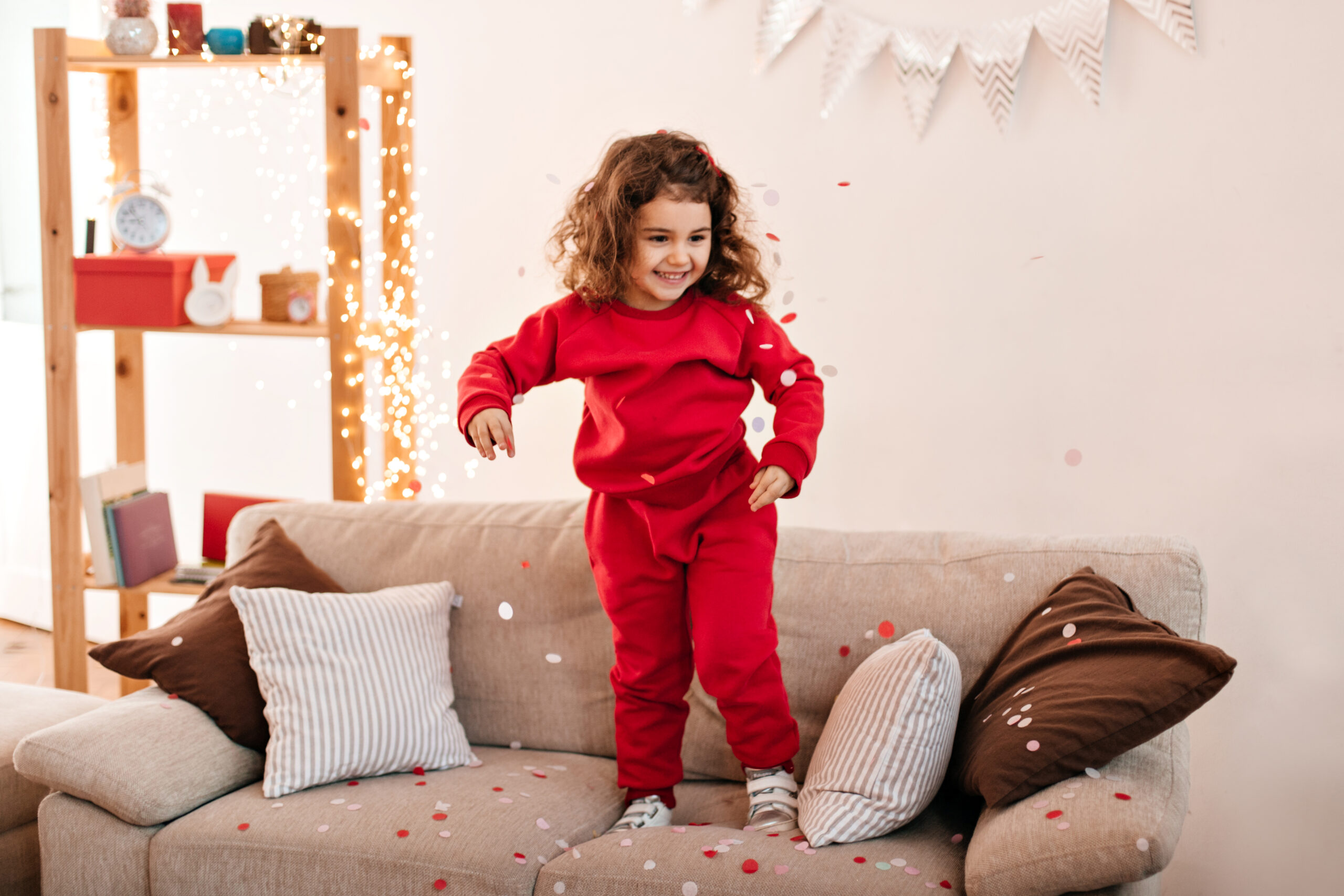 carefree kid in pajama jumping on sofa. brunette little girl standing on couch